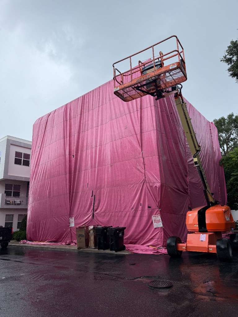 Pink fumigation tent covering a multi-story building with a boom lift raised to the roofline