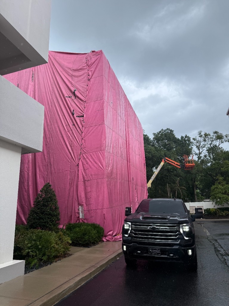 Multi-story building sealed under a bright pink fumigation tent, with a service truck in the foreground