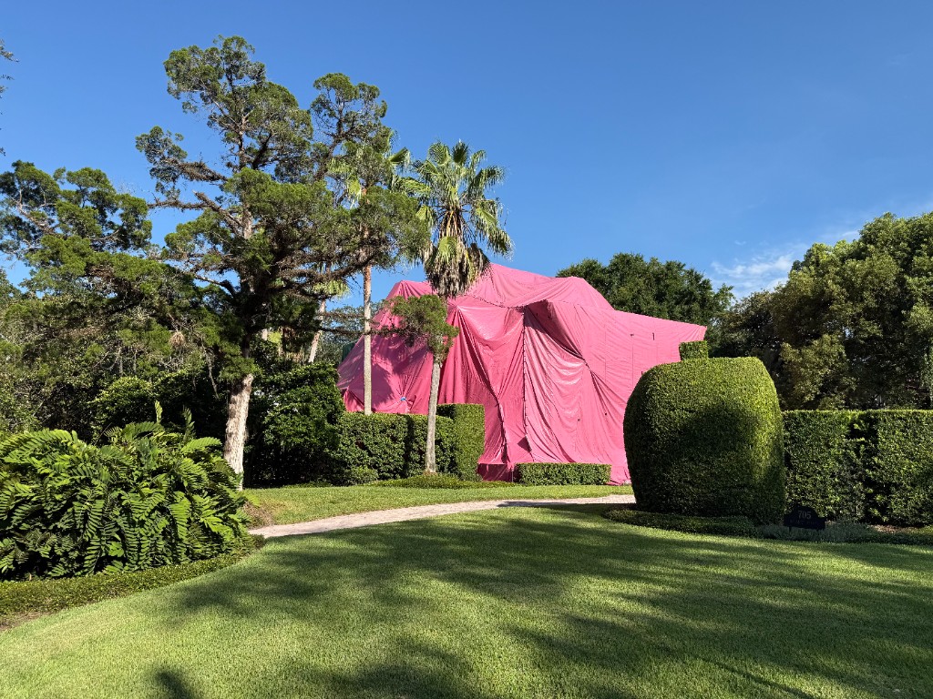 Central Florida home fully sealed under a bright pink fumigation tent, viewed across the front lawn